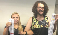 Two students with linked arms each holding up a strip of paper with DNA sequence printed on it.